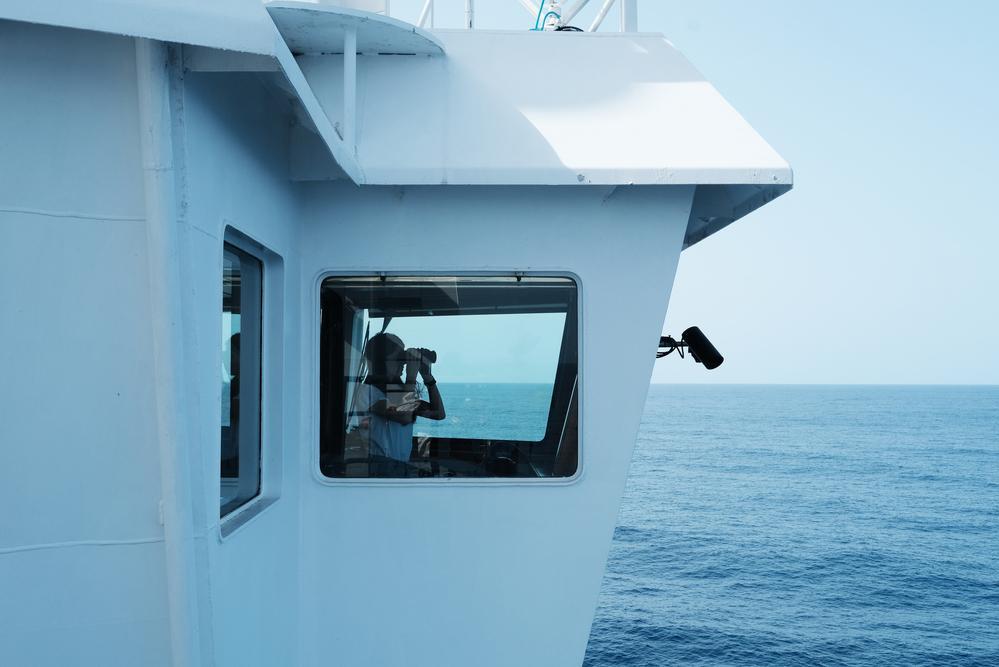 An MSF crew member watches and scans the horizon through his binoculars looking for boats in distress. (Geo Barents, February 2022, @Kenny Karpov)