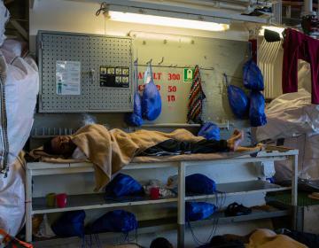 A survivor dozes in the corner of the ‘shelter deck’ (men's deck). (Geo Barents, December 2022, @Mahka Eslami)